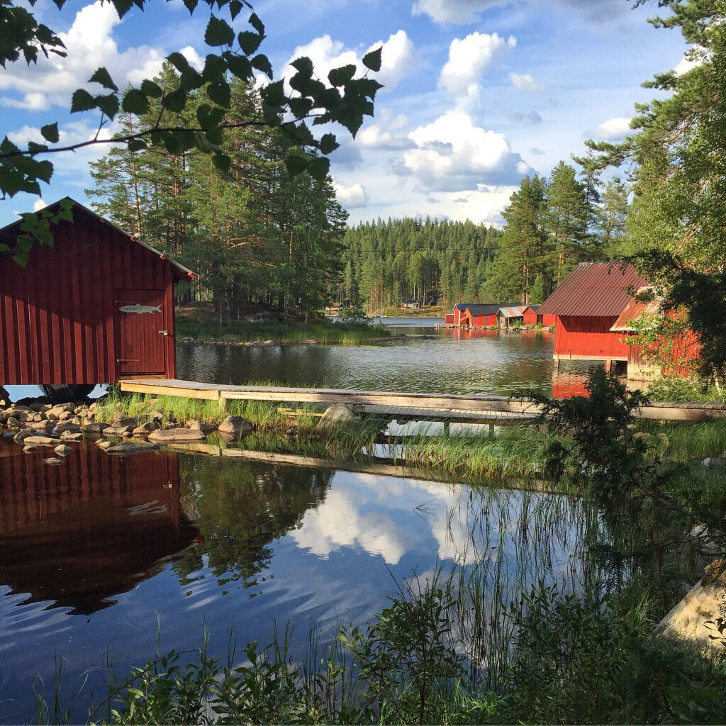 Sjön Gimmen i Dalarna. Röda sjöbodar, en brygga och skog i bakgrunden.