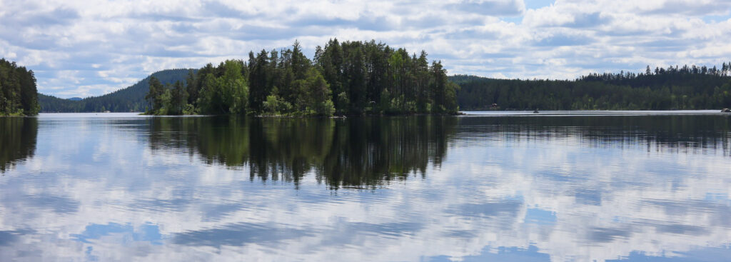 Sjön Gimmen i Dalarna. Spegling av ö i vattnet, blå himmel och vita moln.